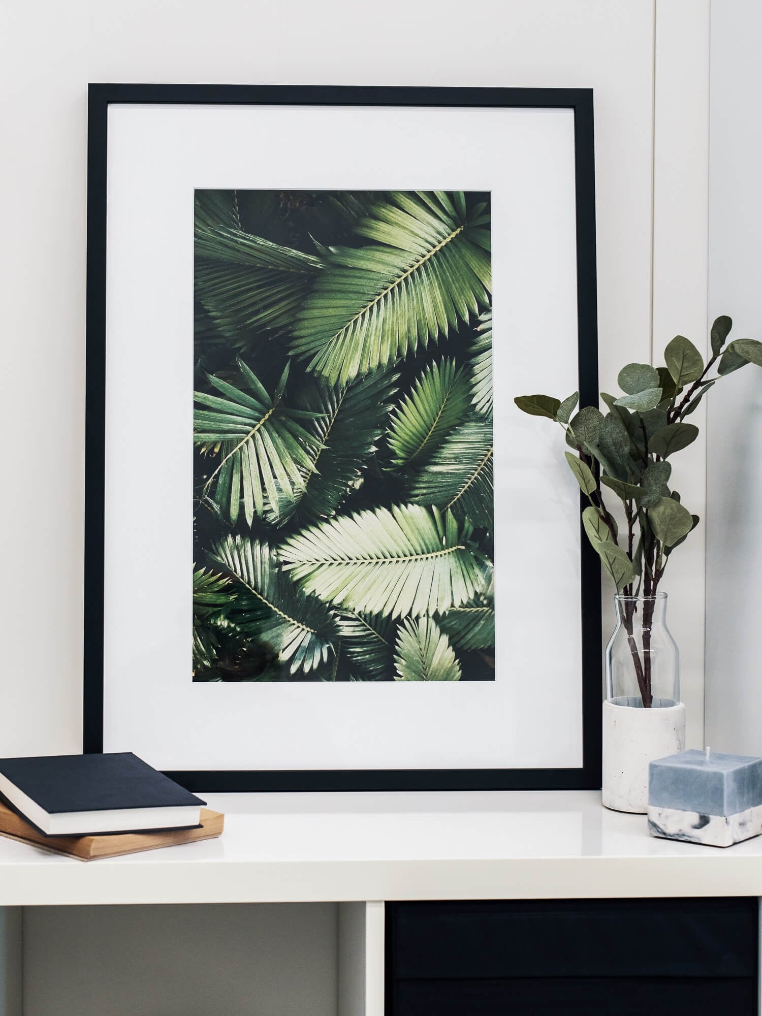 A framed printful poster of tropical palm leaves on a styled shelf