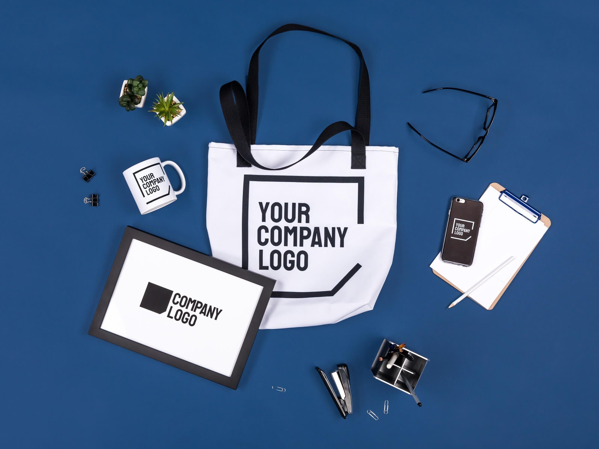 Printful branded tote bag, mug, phone case, and frame on a desk flat lay